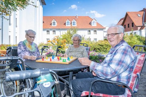 Senioren sitzen an einem Tisch draußen auf der Terrasse und spielen Mensch ärgere dich nicht