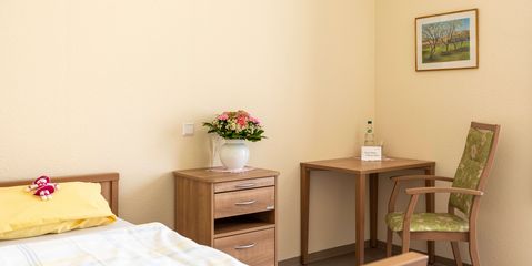 Ihr Zimmer Zimmer mit Bett, Nachttisch, Tisch und Stuhl in der Seniorenresidenz